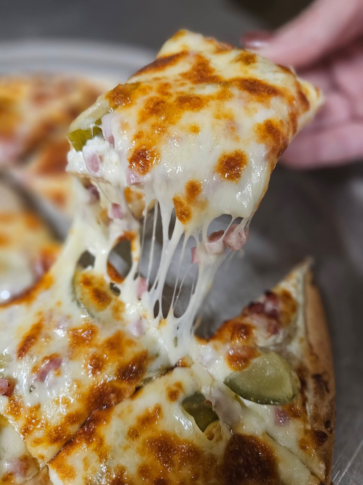 Cheesy slice lifted from a ham and pickle pizza